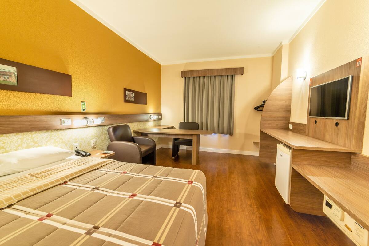 A hotel room with a bed, desk, chair, television, and a small refrigerator.