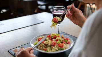 A person dining at a table with a plate of food and a glass of red beverage.