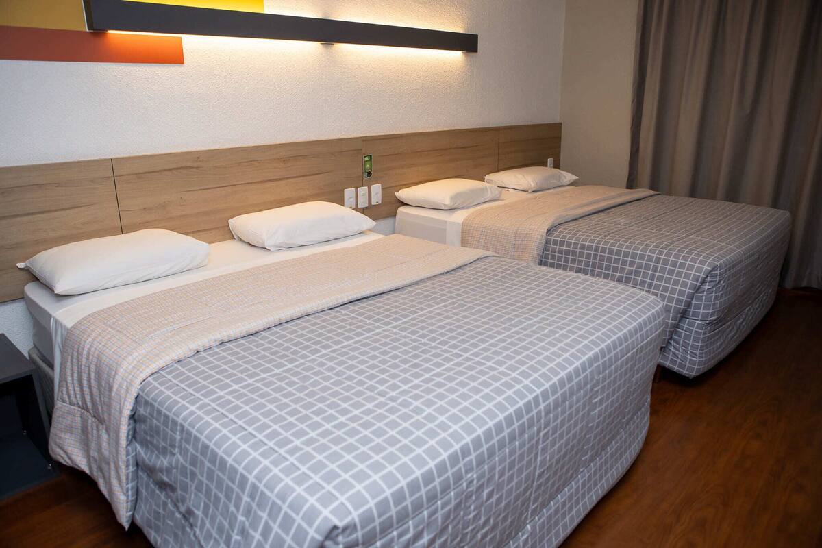 A hotel room with two beds, a wooden headboard, a wall-mounted light, and a curtain.