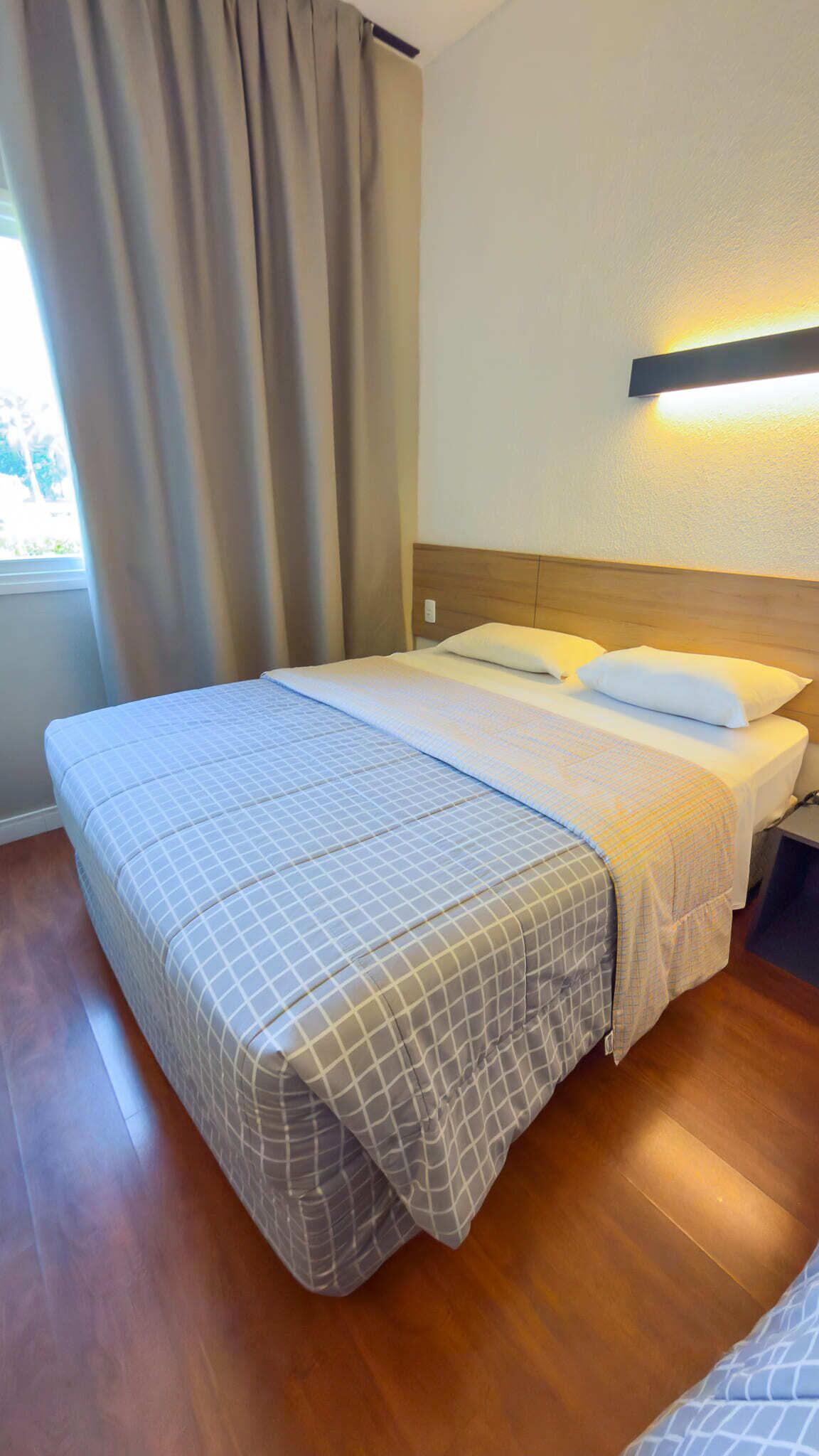 Un lit bien fait, avec une couvre-lit à carreaux, une tête de lit en bois et un luminaire fixé au mur.