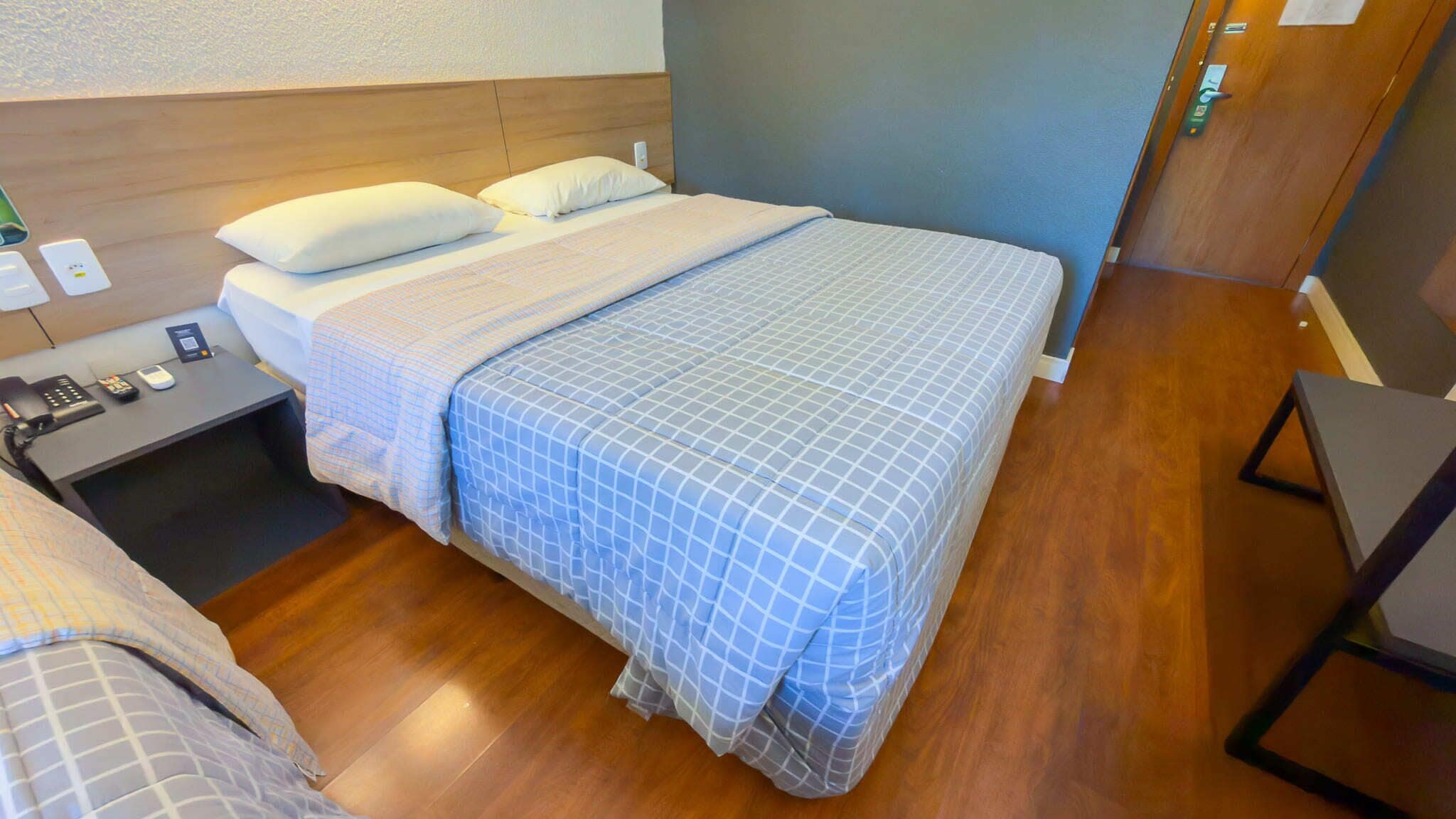 A hotel room with a bed, bedside tables, a phone, and a wall-mounted light.