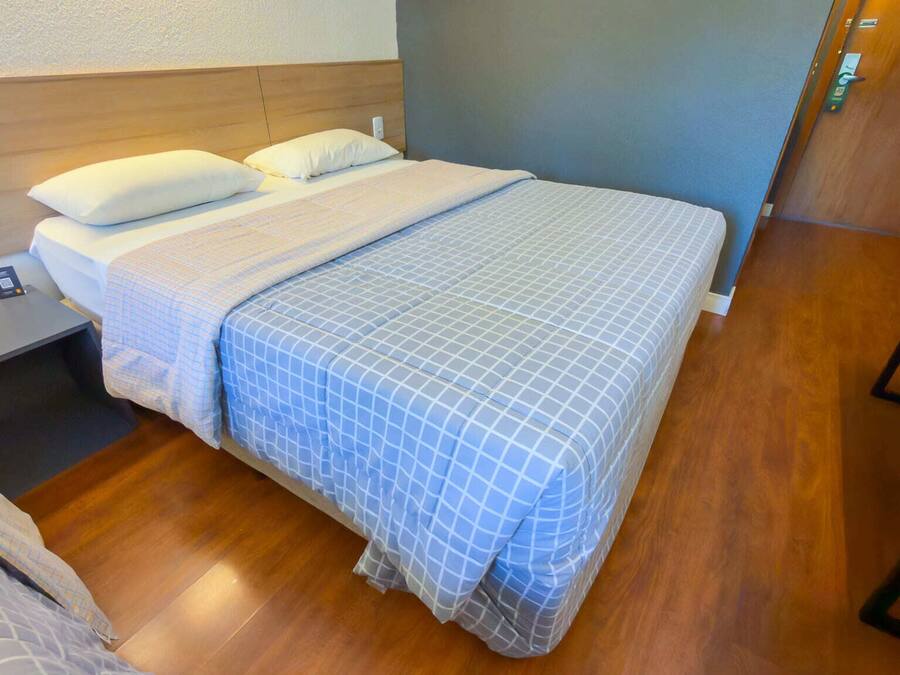 A hotel room with a bed, bedside tables, a phone, and a wall-mounted light.