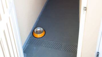Um corredor estreito com uma porta à direita, uma pequena tigela laranja no chão e um marco de porta branco à esquerda.