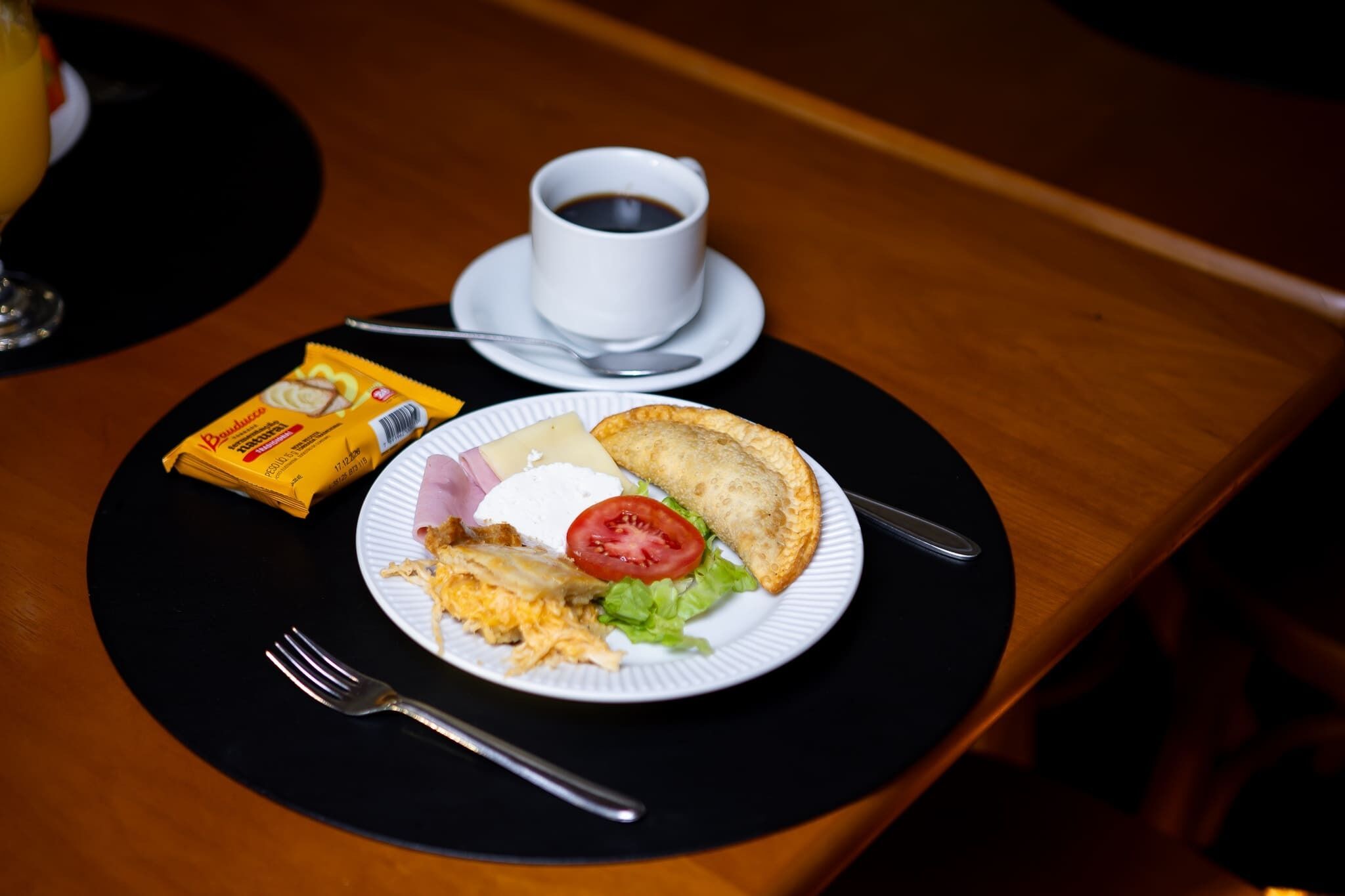Desayuno con un plato de comida, una taza de café y un envase de queso crema.