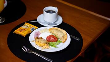 Desayuno con un plato de comida, una taza de café y un envase de queso crema.
