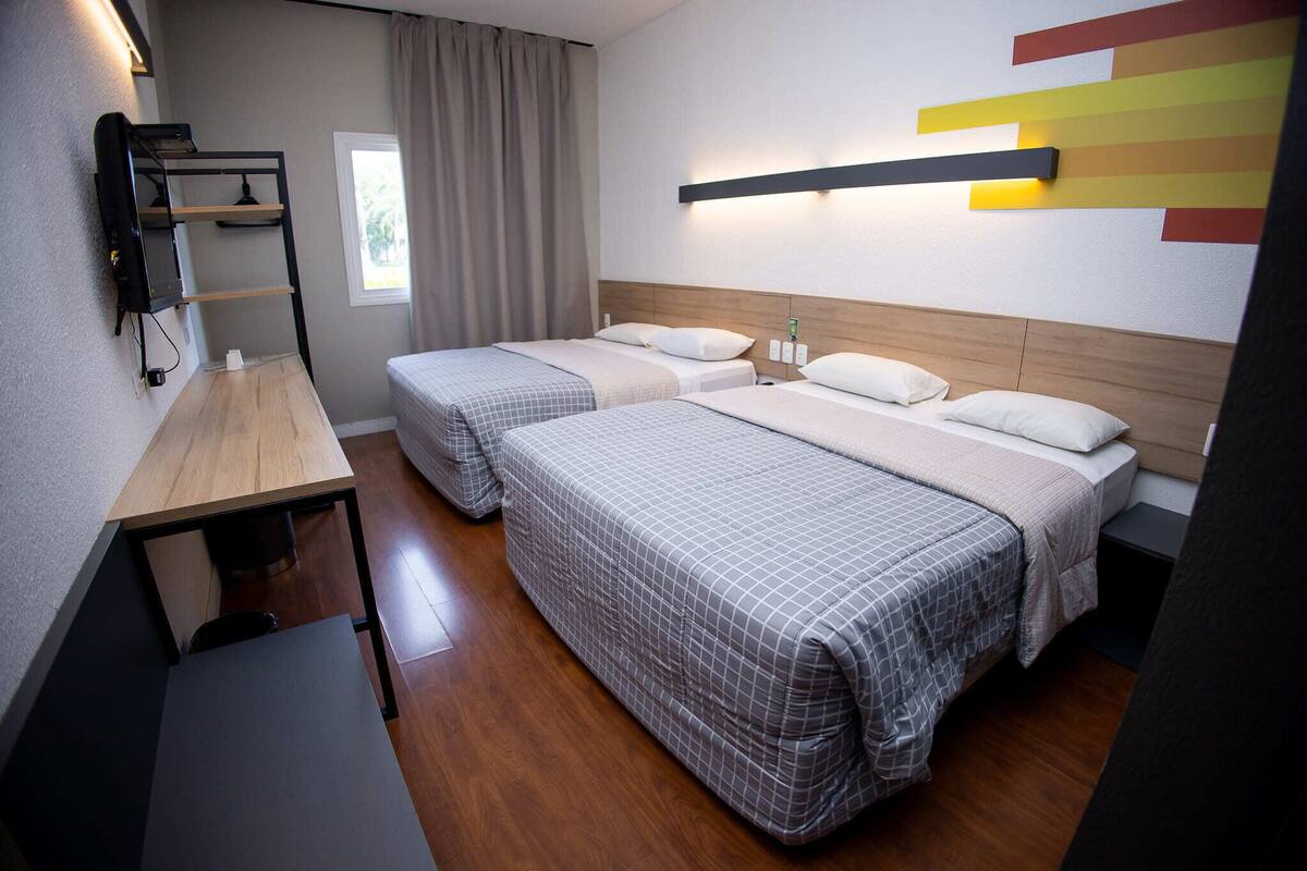 A hotel room with two beds, a desk, a TV, and a window with curtains.