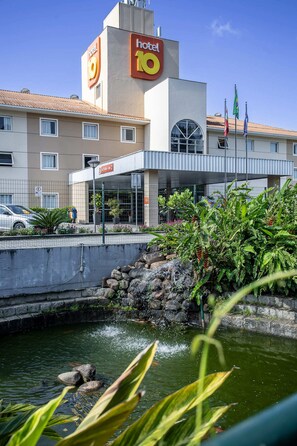 A hotel with a prominent 'hotel 10' sign, a gated entrance, and a small water feature in the foreground.