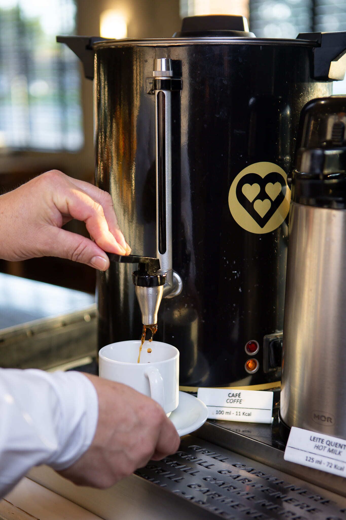 Una persona operando una cafetera, sirviendo café en una taza.
