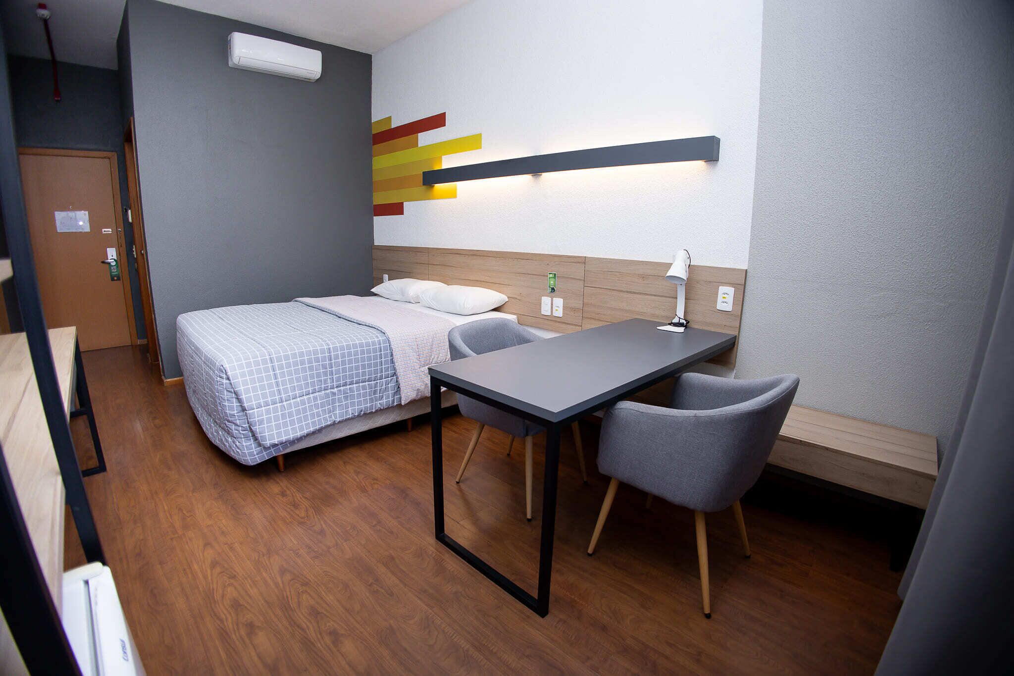 Ein kleines Hotelzimmer mit Bett, Schreibtisch und Stuhl.