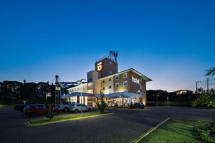 Un hotel con un letrero grande que dice 'hotel', un estacionamiento con varios autos y una entrada bien iluminada.