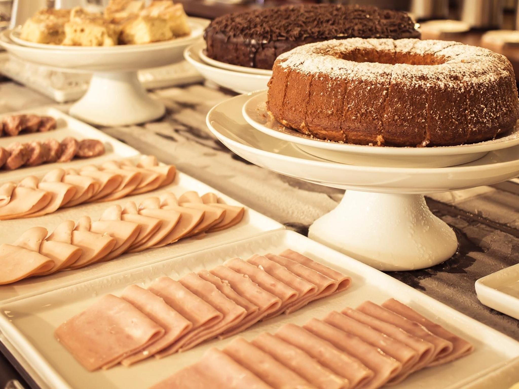 A buffet with various desserts and pastries, including a chocolate bundt cake and neatly arranged pastries on white serving stands.