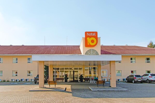 Un hotel con un llamativo letrero que dice 'hotel 10', un acceso cubierto y un área de estacionamiento con automóviles.