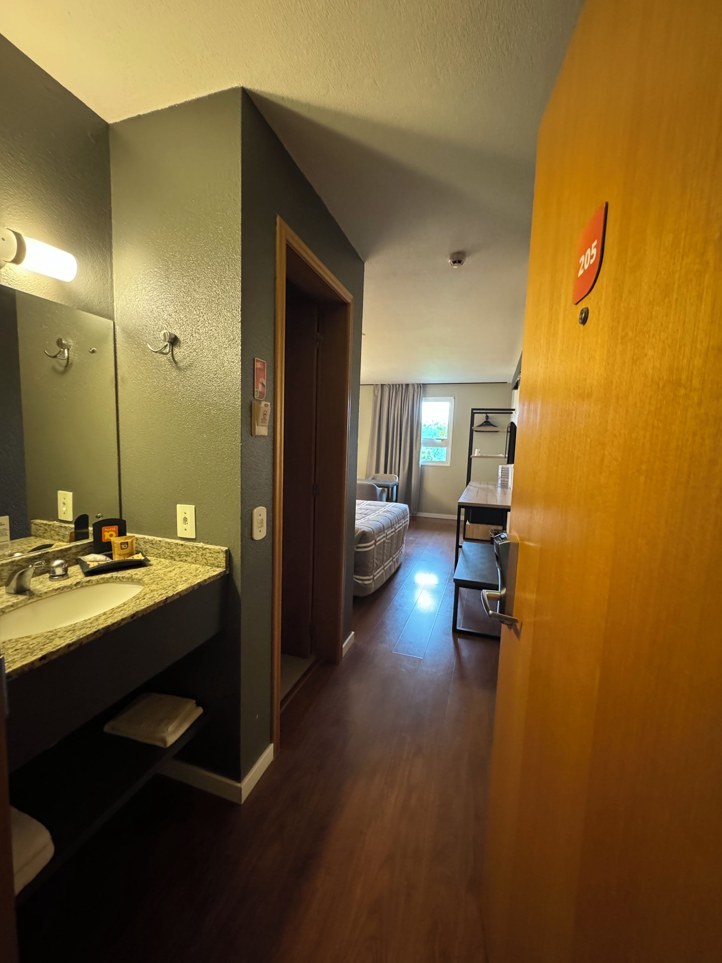 A hotel room with a bathroom, a bed, and a desk.
