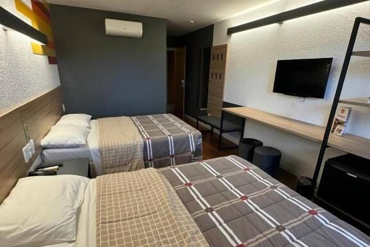 Una habitación de hotel con dos camas, un televisor en la pared y una mesita pequeña.