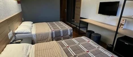 A hotel room with two beds, a TV on the wall, and a small table.