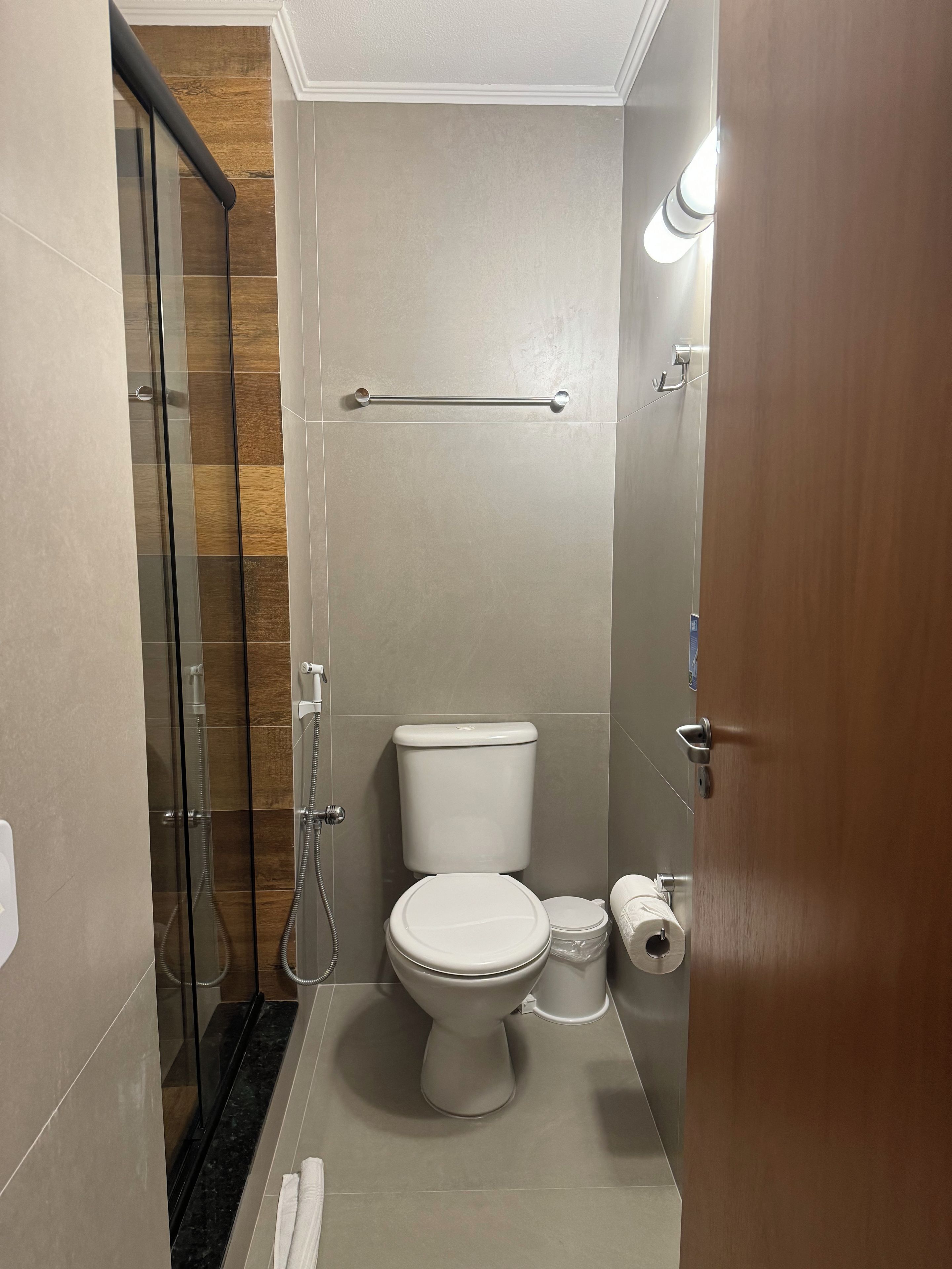 Casa de banho compacta com cabine de chuveiro em vidro, sanita e suporte para toalhas.