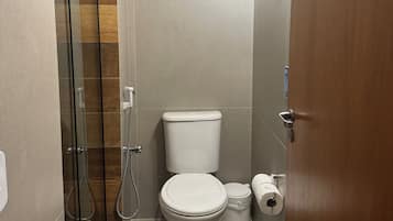 Casa de banho compacta com cabine de chuveiro em vidro, sanita e suporte para toalhas.