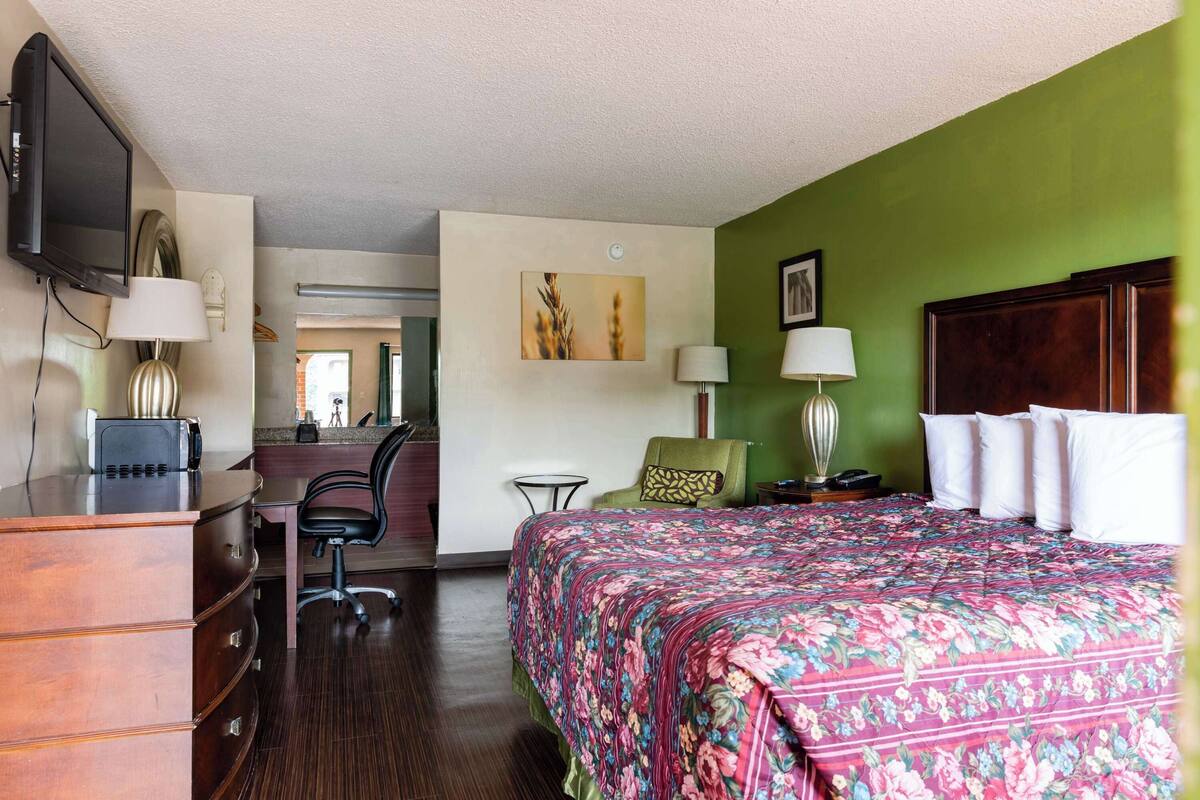 A hotel room with a bed, desk, chair, and a television.