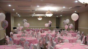 Ein Festsaal mit runden Tischen, die mit rosa Tischdecken bedeckt sind, Stühlen mit rosa Bändern und Luftballons.
