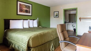 Ein Hotelzimmer mit einem Bett, einem Sessel, einem Schreibtisch und einem durch eine offene Tür einsehbaren Badezimmer.