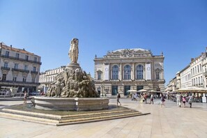 Une place publique avec une fontaine centrale et un bâtiment historique en arrière-plan.