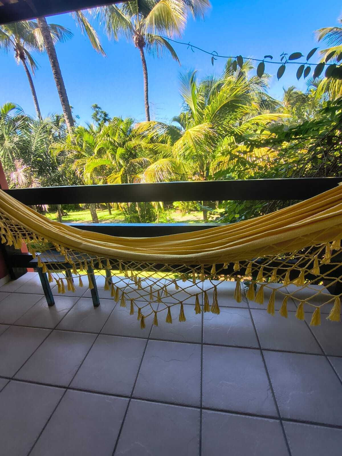 A hammock on a tiled patio with a view of palm trees and greenery.
