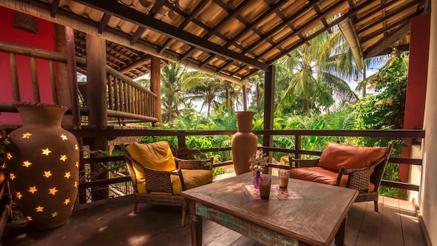 An outdoor seating area with wicker furniture and a wooden table, surrounded by lush greenery and a thatched roof structure. - Porto Zarpa Hotel (Mata de São João)