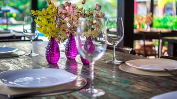 Mesa posta com pratos, talheres e vasos de vidro rosa com flores.