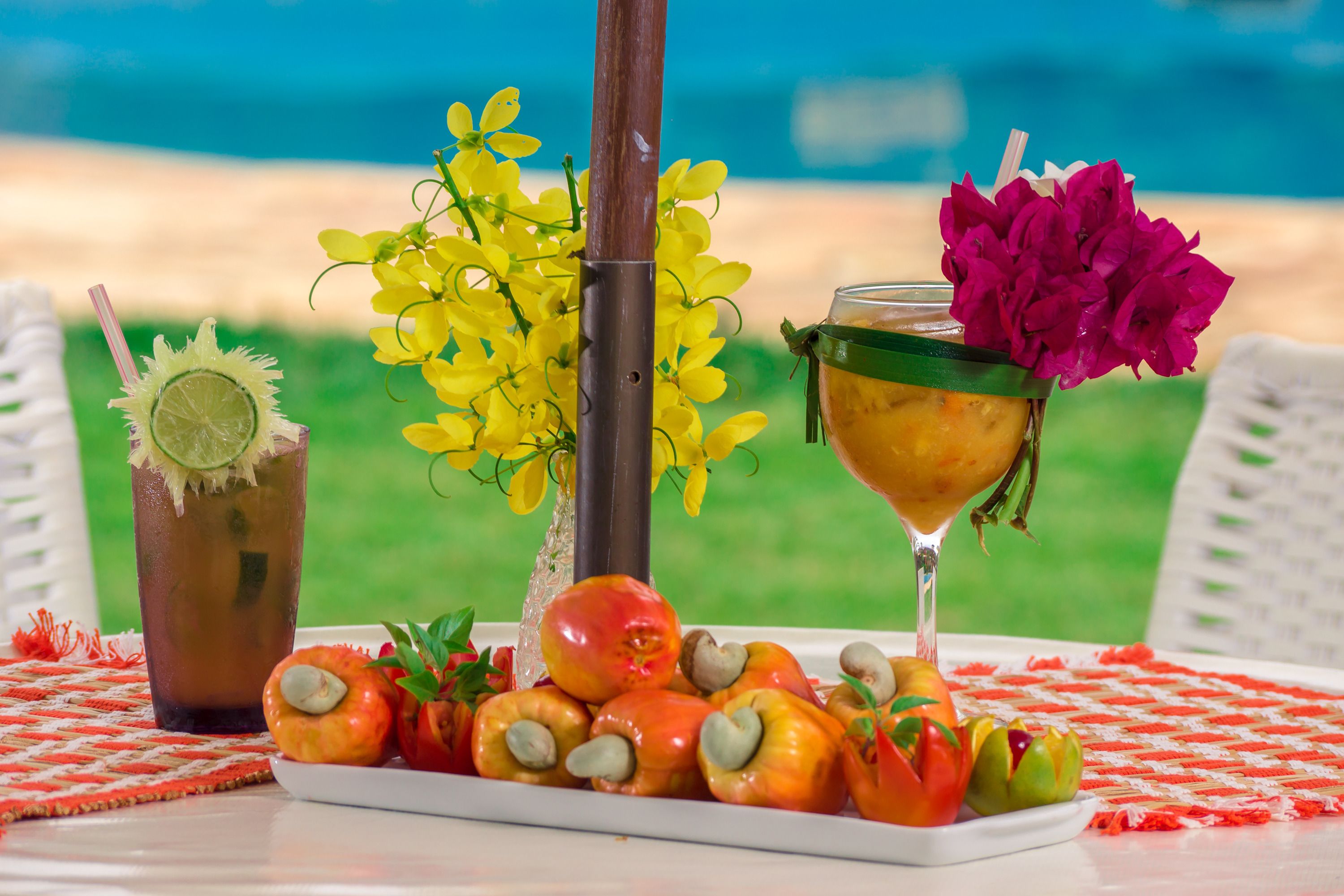 Una mesa con una bebida, un plato de pimientos rellenos y un florero con flores.