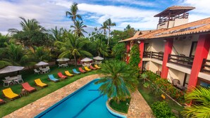 A pool area with lounge chairs and umbrellas, surrounded by palm trees and a building with a tiled roof. - Porto Zarpa Hotel (Mata de São João)