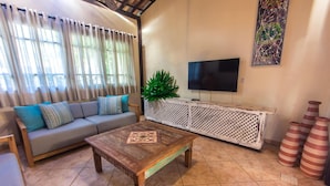 A living room with a sofa, coffee table, TV, and decorative vases. - Porto Zarpa Hotel (Mata de São João)