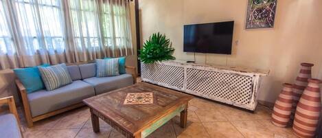 Una sala de estar con sofá, mesa de centro, televisor y jarrones decorativos.