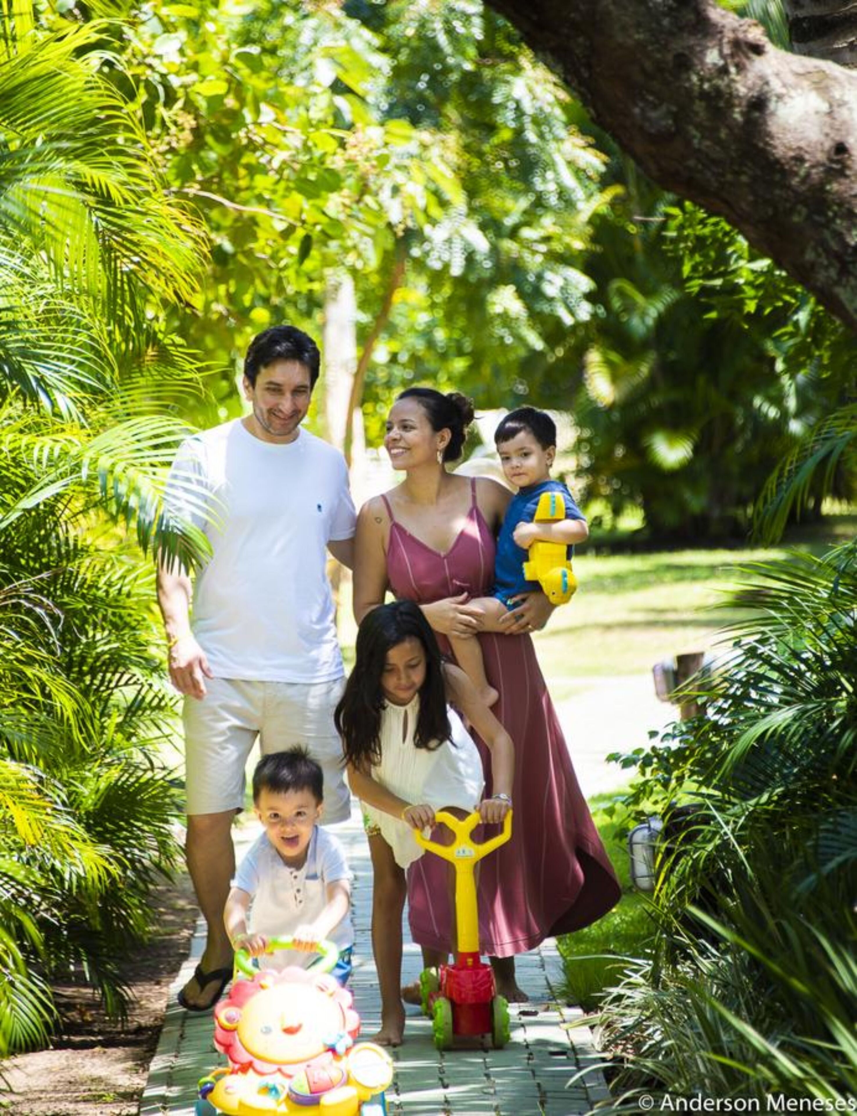 Uma família caminhando em um jardim exuberante com palmeiras e um caminho pavimentado.