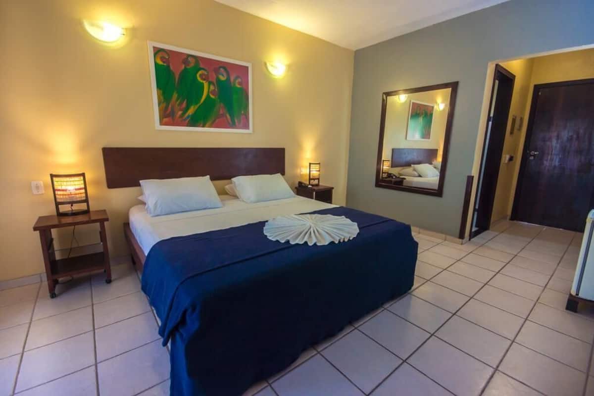 Una camera d'albergo con un letto grande, due comodini, uno specchio fissato alla parete e un quadro sopra il letto.