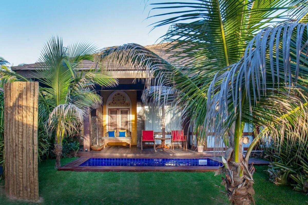 Ein Poolbereich mit Holzterrasse, einer Sitzgruppe mit Bank und Stühlen sowie einer Palme im Vordergrund.