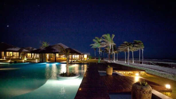 A nighttime resort pool area with overwater bungalows and palm trees. - Zorah Beach Hotel (Trairi)