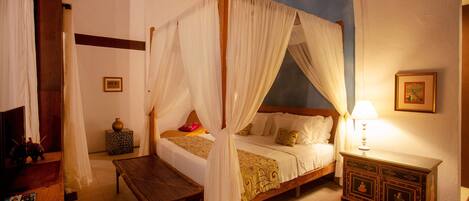 A four-poster canopy bed with a nightstand and a wooden bench.