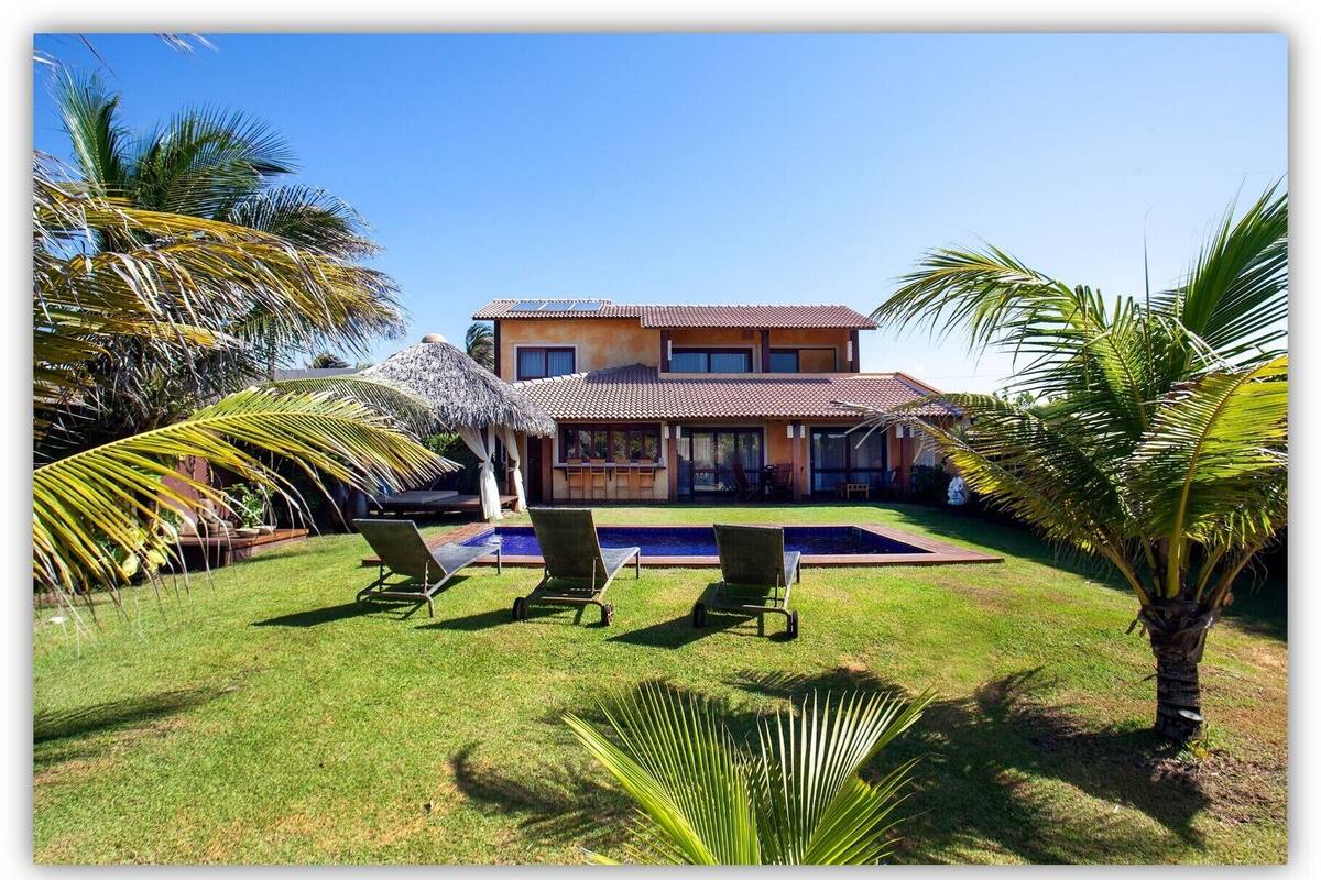 Ein zweistöckiges Haus mit Swimmingpool, umgeben von Palmen und einem gepflegten Rasen.