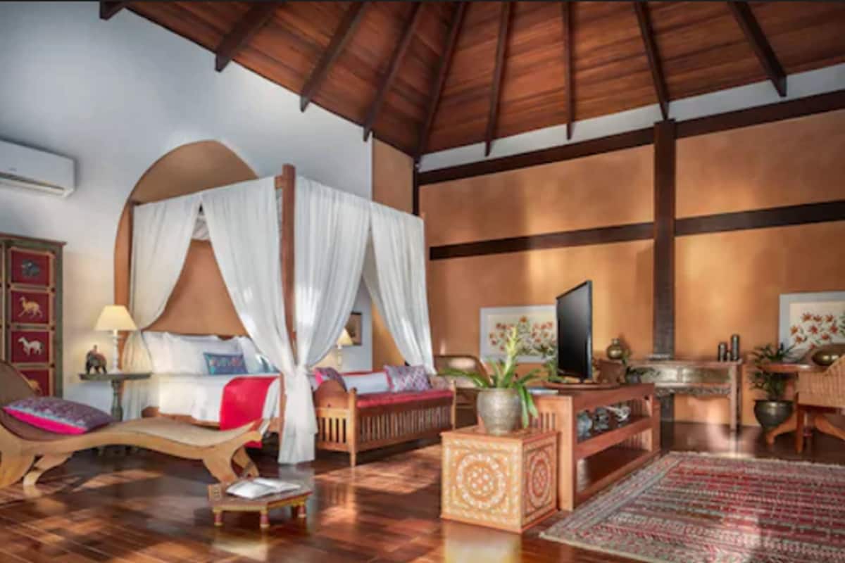 Ein geräumiges Zimmer mit einem großen Bett, einem Fernseher und einer Holzbalkendecke.