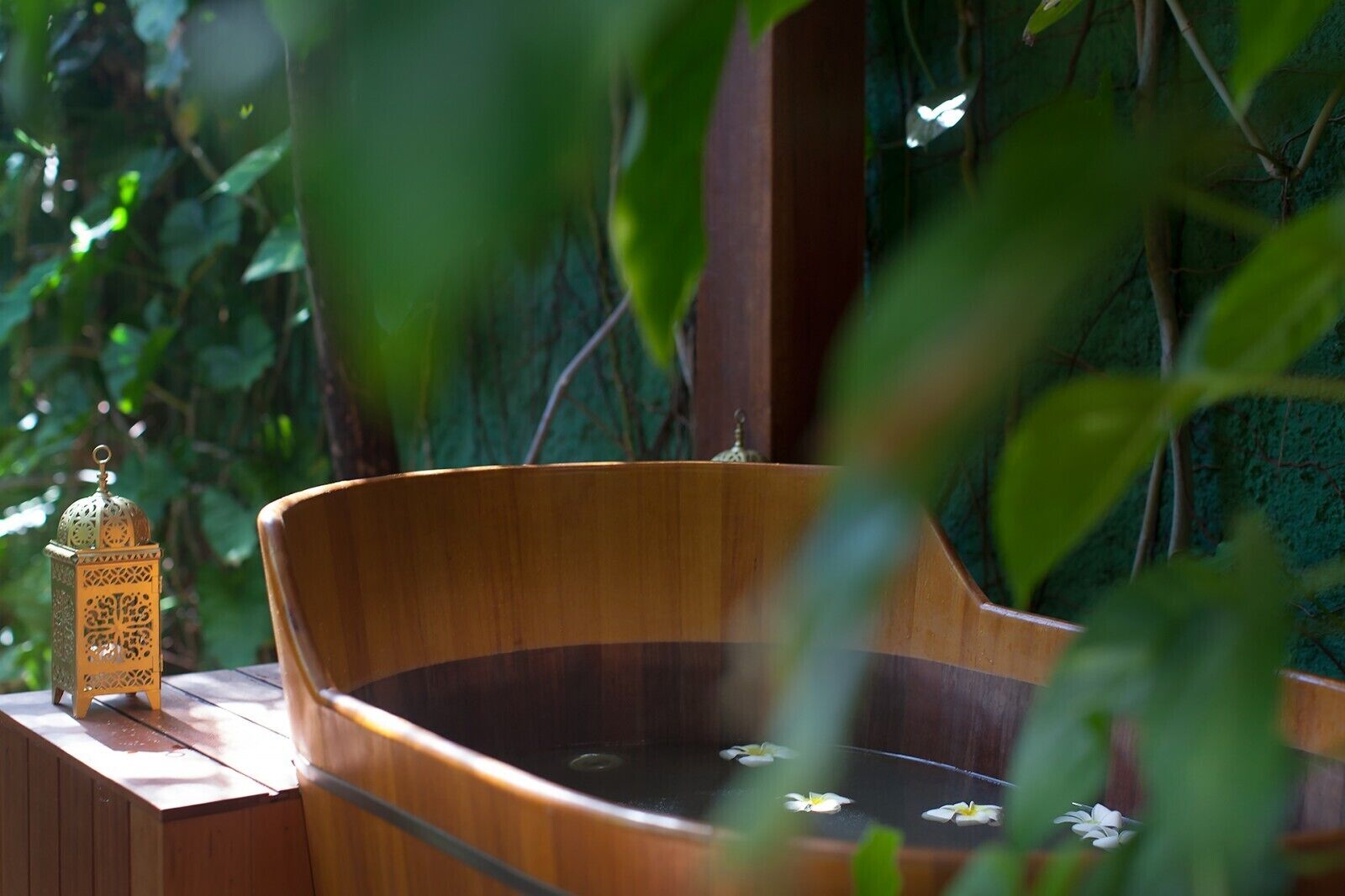 A wooden hot tub with a decorative lantern beside it, surrounded by lush greenery.