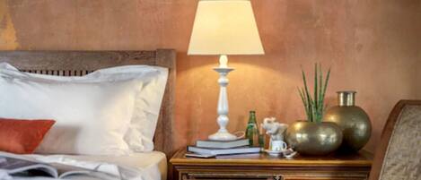 Una cama bien hecha con almohadas blancas y rojas, una mesita de noche con lámpara, libros y objetos decorativos.