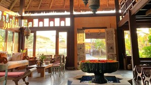A spacious indoor area with a high thatched roof, wooden furniture, and a central water feature. - Zorah Beach Hotel (Trairi)