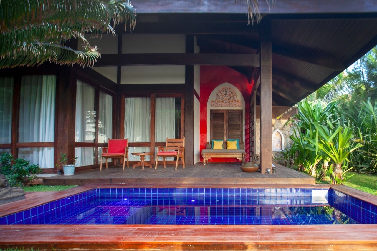 A pool area with a tiled blue pool, wooden deck, and a covered seating area with chairs and cushions.