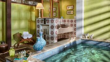 Zona de spa con piscina, mesa de masaje y diversos servicios, incluyendo botellas y un jarrón azul.