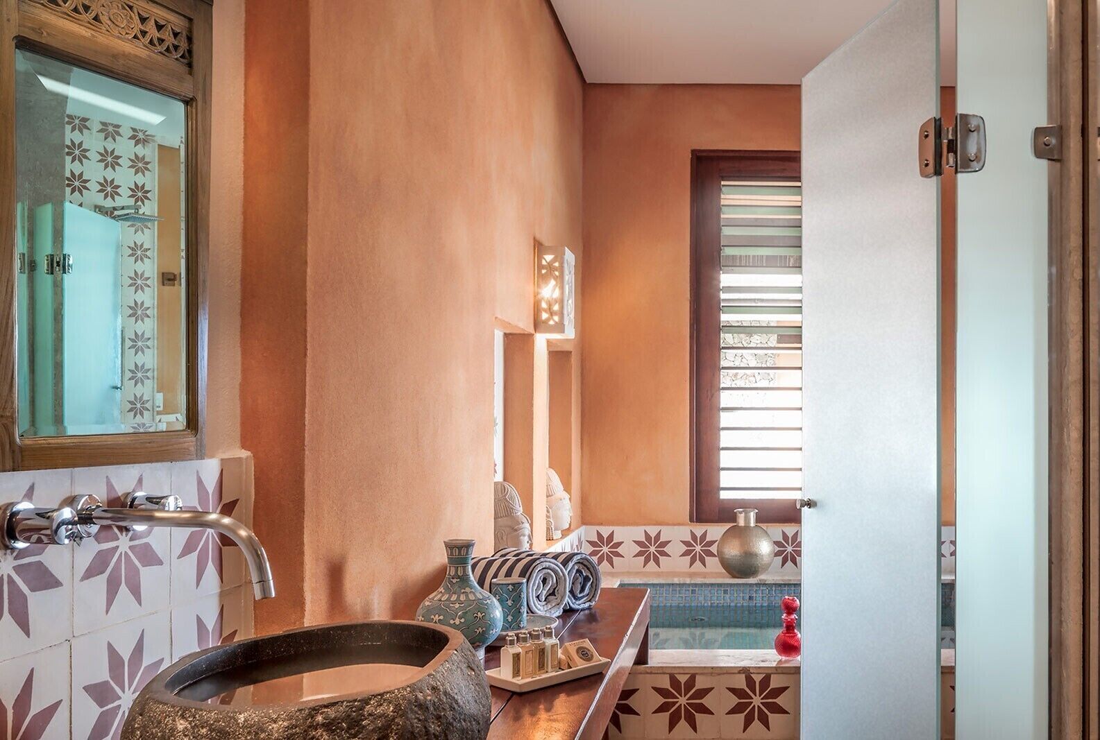 A bathroom with a stone basin, a mirror, and a window with blinds.