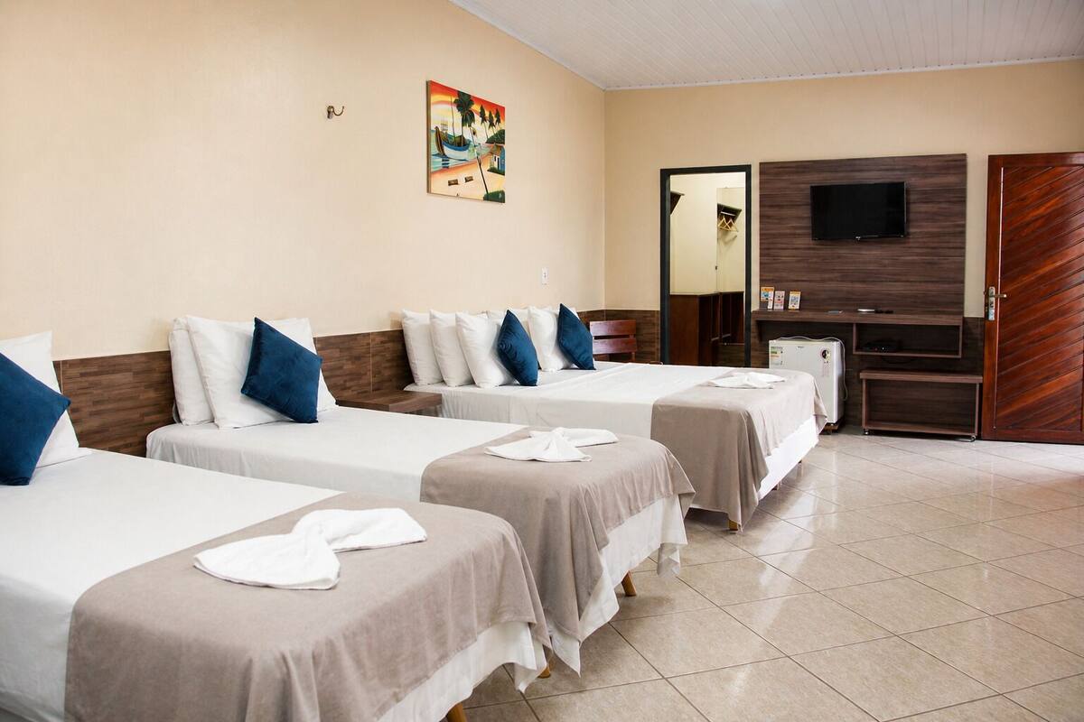 Une chambre d’hôtel avec quatre lits simples, une télévision, un minibar et une porte en bois.