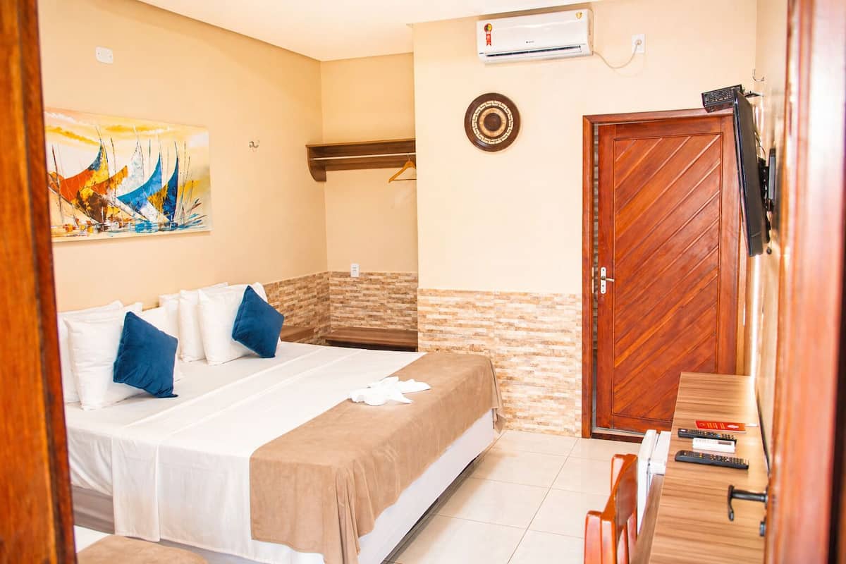 Une chambre d’hôtel avec un lit, une porte en bois, un climatiseur fixé au mur et un tableau.