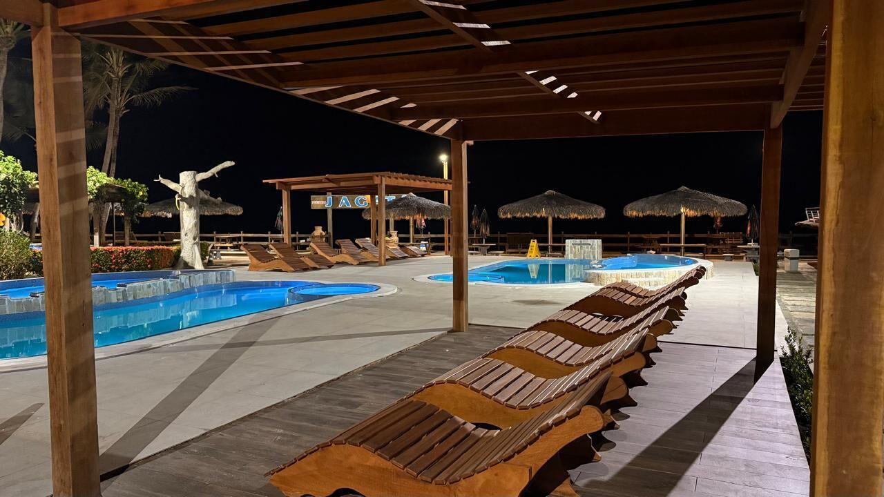 A pool area with lounge chairs and umbrellas, a covered seating area, and a sign that reads "JAGUAR".