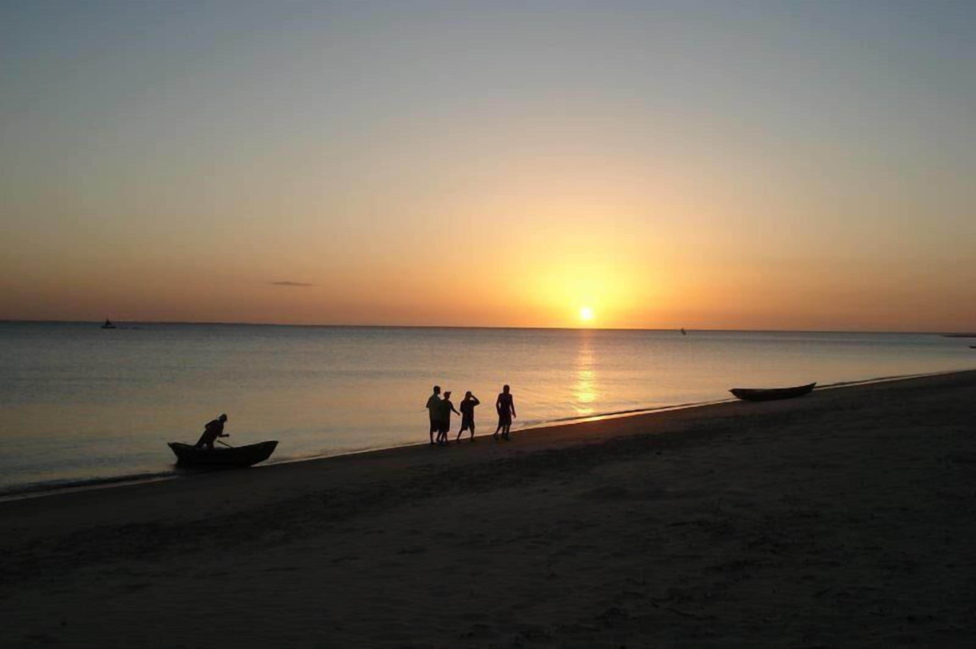 Una playa al atardecer con algunas personas y barcos.