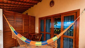 Una habitación con techo de madera, una hamaca, una puerta de madera y vistas, y una silla.